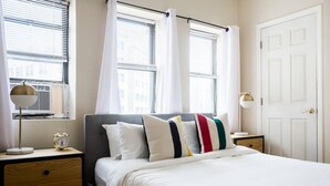Une chambre à coucher bien rangée, avec un lit, deux tables de chevet, une commode, une lampe et une fenêtre équipée de stores.