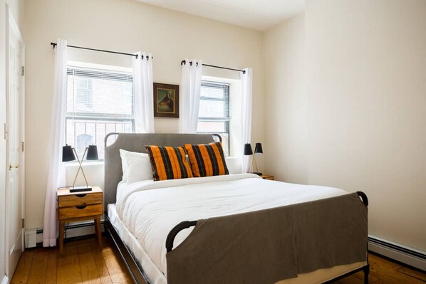 A bedroom with a bed, nightstands, a window with curtains, and a picture on the wall.