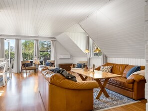 Un loft espacioso con techo alto, una mesa de comedor de madera, sofás de cuero y grandes ventanales que ofrecen vistas al exterior.