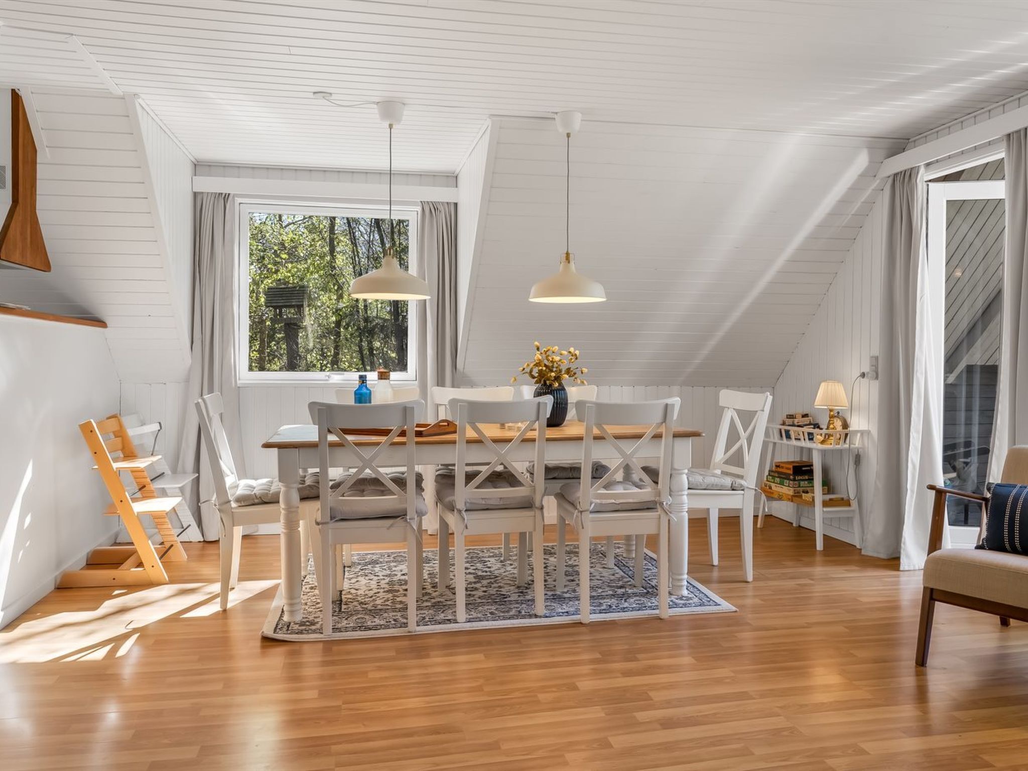 Et spiseområde med et træbord, hvide stole og en hængende lampe.