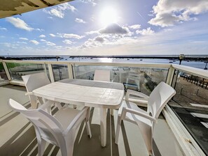 Ein Balkon mit Tisch und Stühlen, mit Blick auf einen Strand mit Booten und einem Steg.