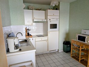 Une cuisine compacte avec des meubles blancs, un four encastré, un four à micro-ondes et une machine à café.