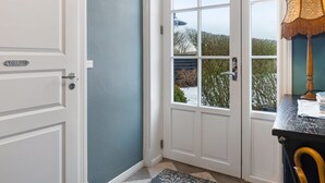 Eine Tür mit weißem Rahmen und einer Beschriftung, ein Fenster mit Blick auf Bäume und eine verschneite Landschaft sowie ein Tisch mit einer Lampe und einem Buch.