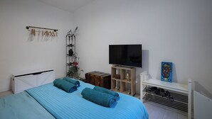 Une chambre à coucher avec un lit, une télévision, une étagère avec un cadre photo et un radiateur.