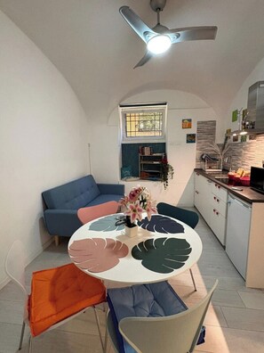 A compact living space with a dining table, chairs, a sofa, a ceiling fan, a kitchen area, and a window with a view. - [Colosseum - Esquilino] Ikigai Peaceful Apartment (Roma)