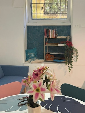 A room with a window, a bookshelf, a blue sofa, and a table with a vase of flowers. - [Colosseum - Esquilino] Ikigai Peaceful Apartment (Roma)