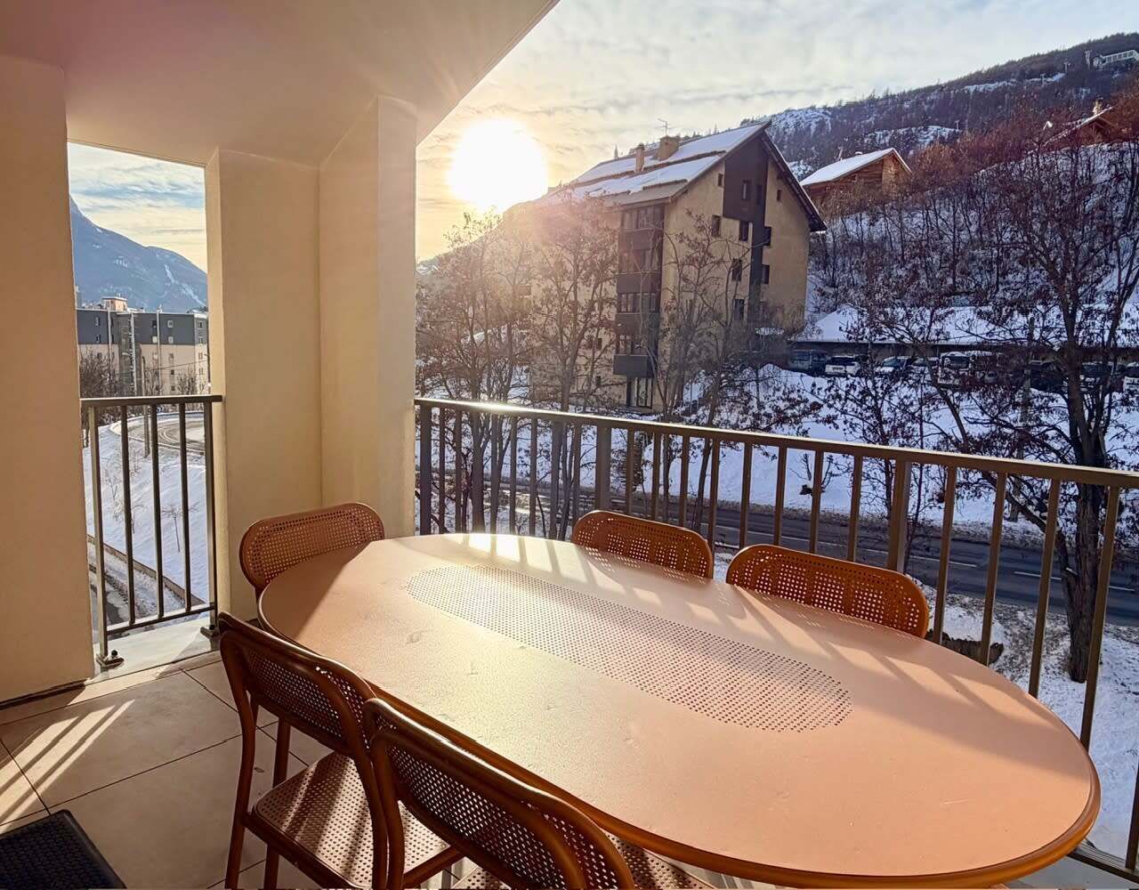 A balcony with a table and chairs, overlooking a snowy landscape and buildings.