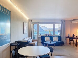 Ein modernes Wohnzimmer mit einer Couch, einem runden Tisch und Blick auf einen See und Berge.
