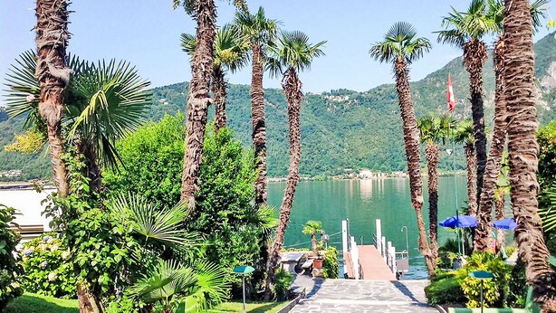 A pathway leading to a dock with palm trees and a lake view. - Blue Vista Lugano Apt.616 by Interhome (Bissone)