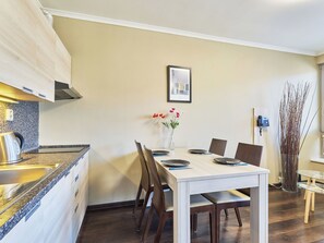 Una cuina moderna amb fornel integrat, taula de dinar amb caires i un vas amb flors a la paret.