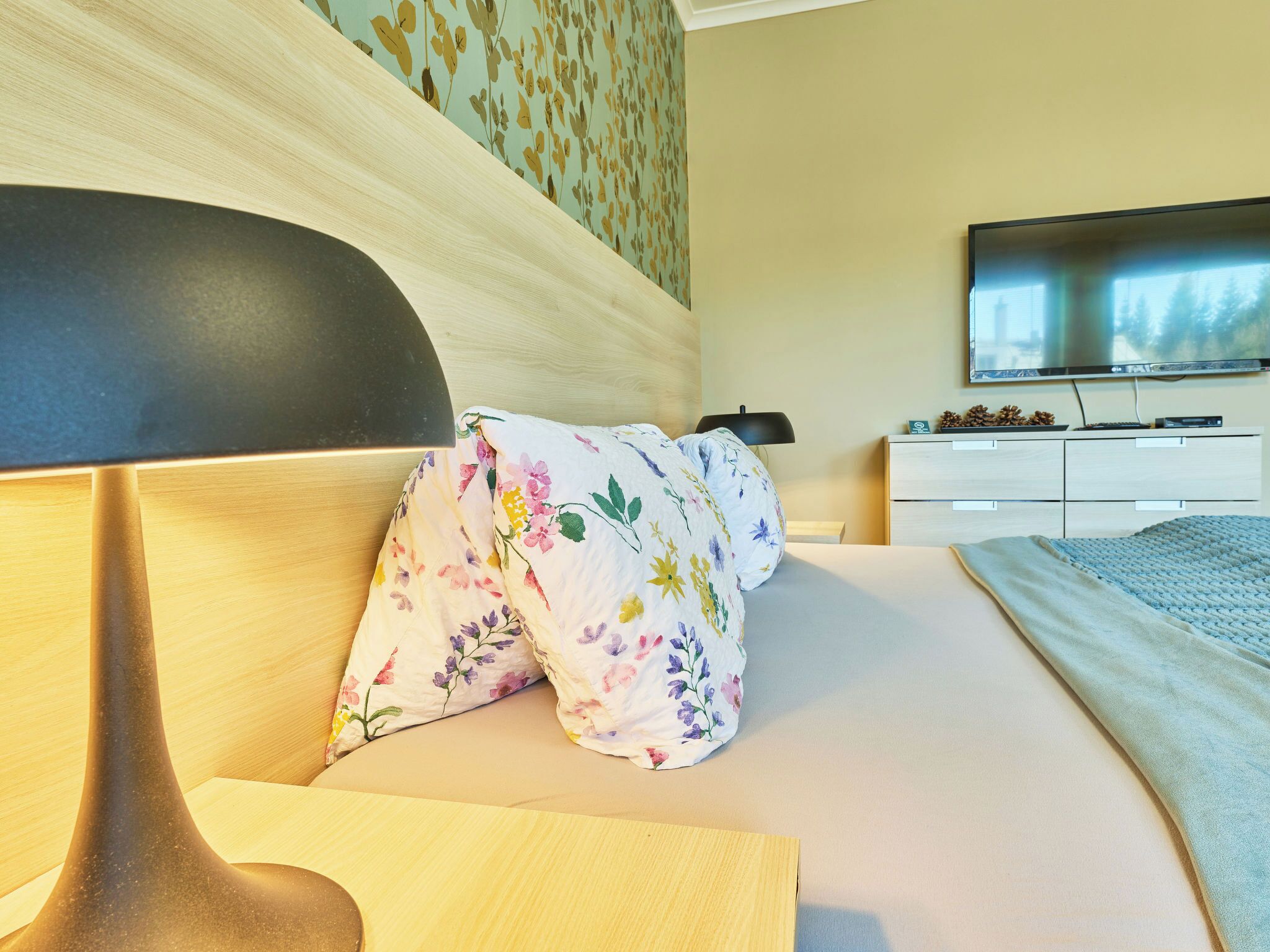 Ein Hotelzimmer mit Bett, Nachttisch, Lampe, Fernseher und Kommode.