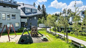 En modern bostadsbyggnad med en lekplats, en grön gräsmatta och en gångstig.