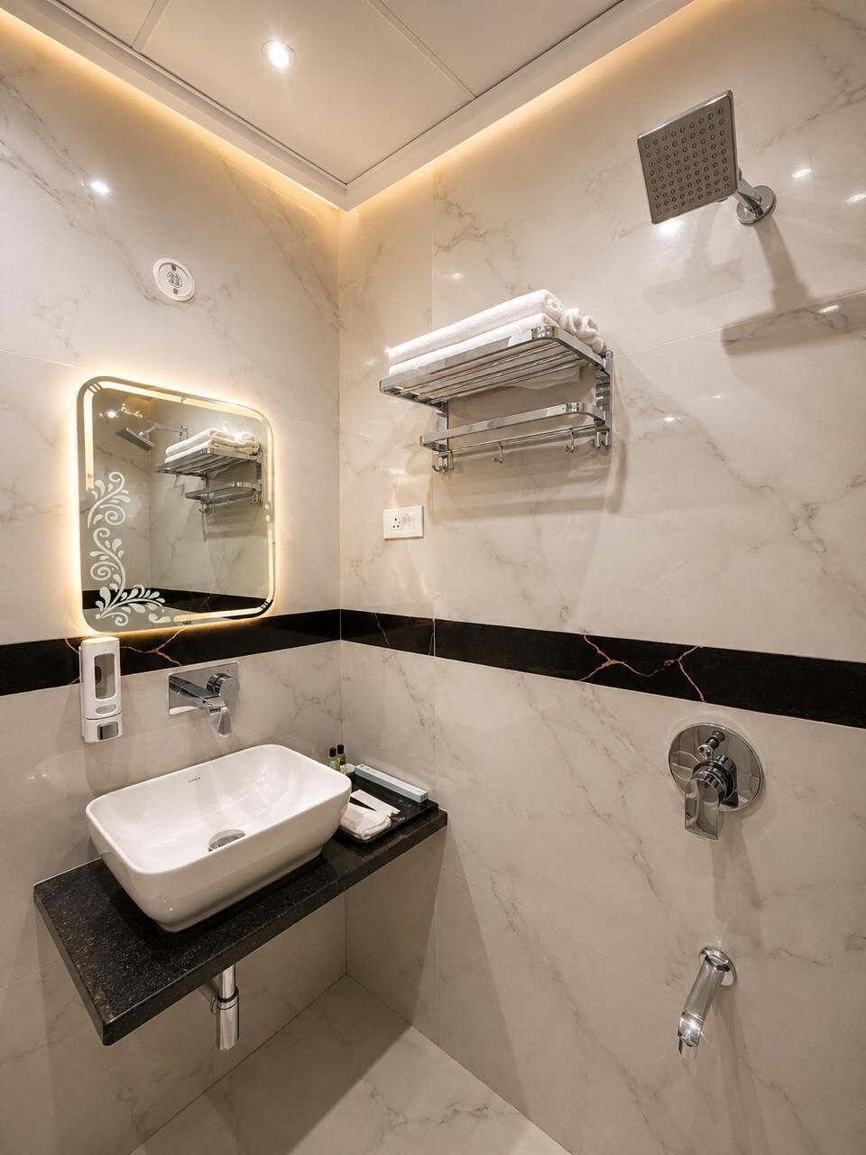 A bathroom with a white sink, a mirror with lights, a shower, and towel racks.