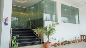 A staircase leading to an interior space with glass walls, a fire extinguisher on the wall, and multiple potted plants. - Hotel KS Palace (Sarnath)