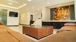 A modern living room with a glass coffee table, leather sofas, a mounted TV, and a large Buddha painting. - Hotel KS Palace (Sarnath)