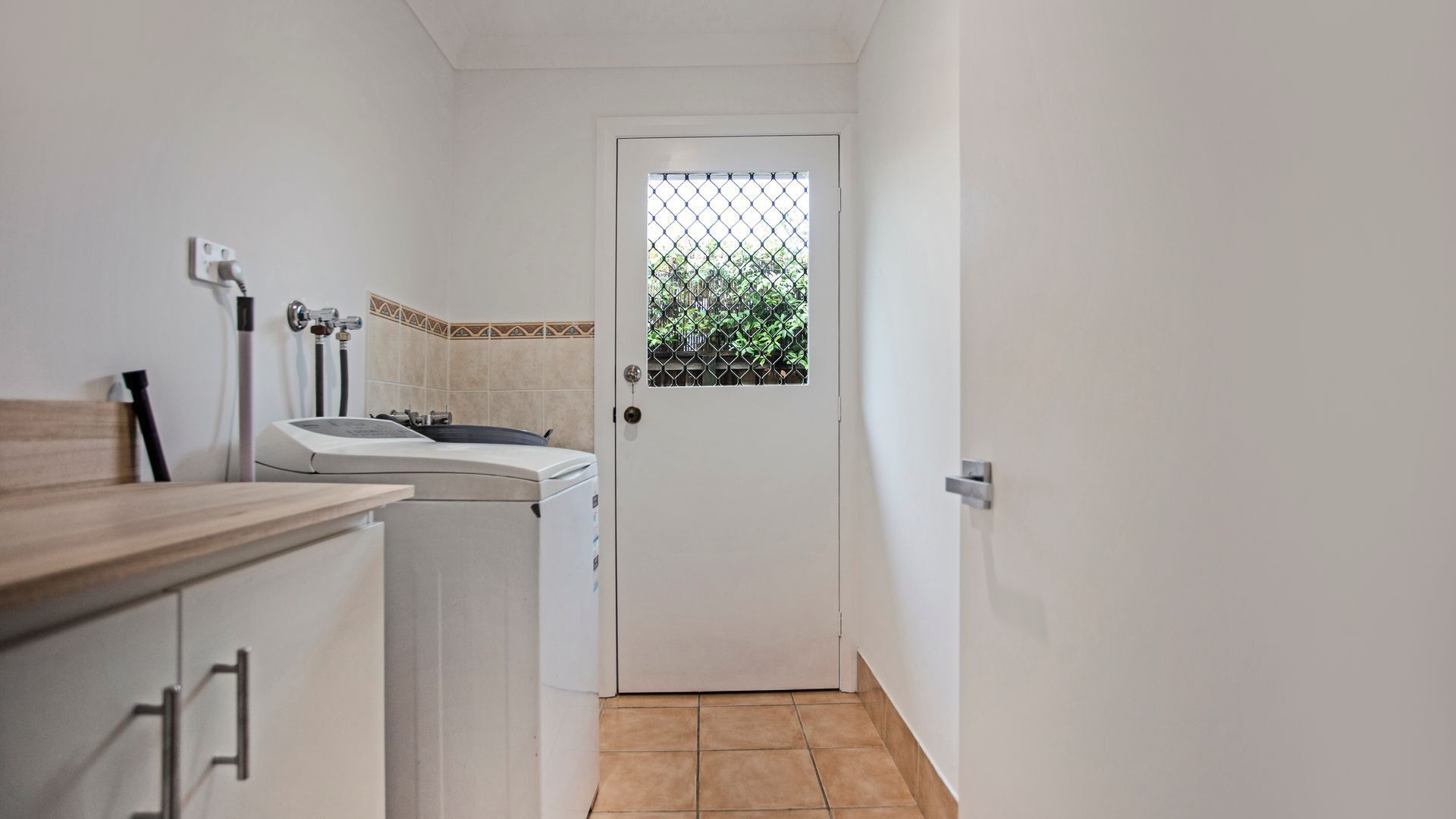 A laundry room with a washing machine, a dryer, and a small window with a view of greenery.