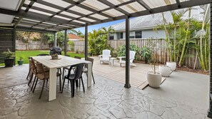 A covered patio with a stone floor, a table with chairs, and potted plants. - The Lazy Pelican - Tea Gardens (Tea Gardens)