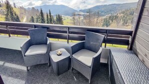 Un balcone con sedie in vimini e un tavolino, con vista su un paesaggio montuoso.