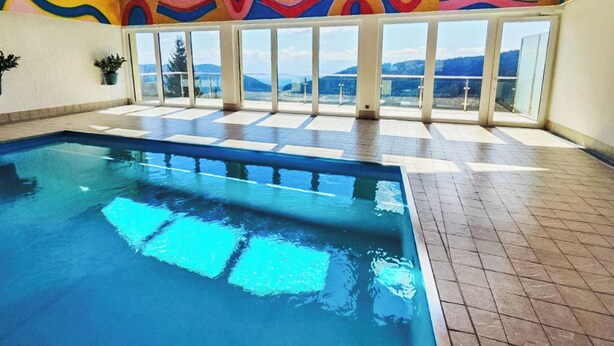 Una piscina interna con vista diretta sulle montagne grazie a ampie finestre.