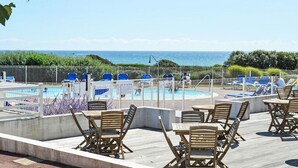 Un espace aménagé au bord de la piscine, avec des chaises longues et des tables, une piscine et une vue sur l’océan.
