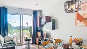 Un salon moderne avec un coin repas, de grandes portes-fenêtres coulissantes donnant sur un balcon et une vue sur l’extérieur.