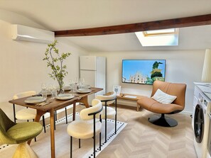 Un soggiorno moderno con zona pranzo, divano, lavatrice e un'ampia finestra vista sulla città.