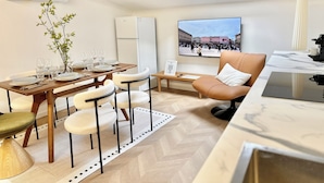 Ein moderner Essbereich mit einem Holztisch, gedeckt für vier Personen, einer Couch und einem Fernseher, der das Piazza Duomo zeigt.