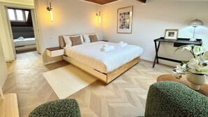 Ein modernes Schlafzimmer mit Holzboden, einem großen Bett, Nachttischen, einem Schreibtisch und einer kleinen Pflanze.