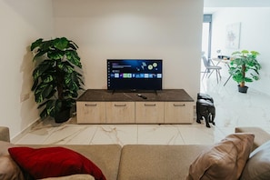 A living room with a TV on a wooden cabinet, a large plant, and a statue on the floor. - Luxurious 2-bedroom apartment with Backyard in Sliema (Tas-Sliema)