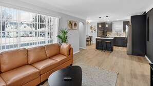 Een moderne woonkamer met een leren bank, een eethoek en een keuken met donkere kastjes en een licht houten vloer.