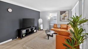 Een moderne woonkamer met een flatscreen televisie, een bank, een salontafel en een grote plant.