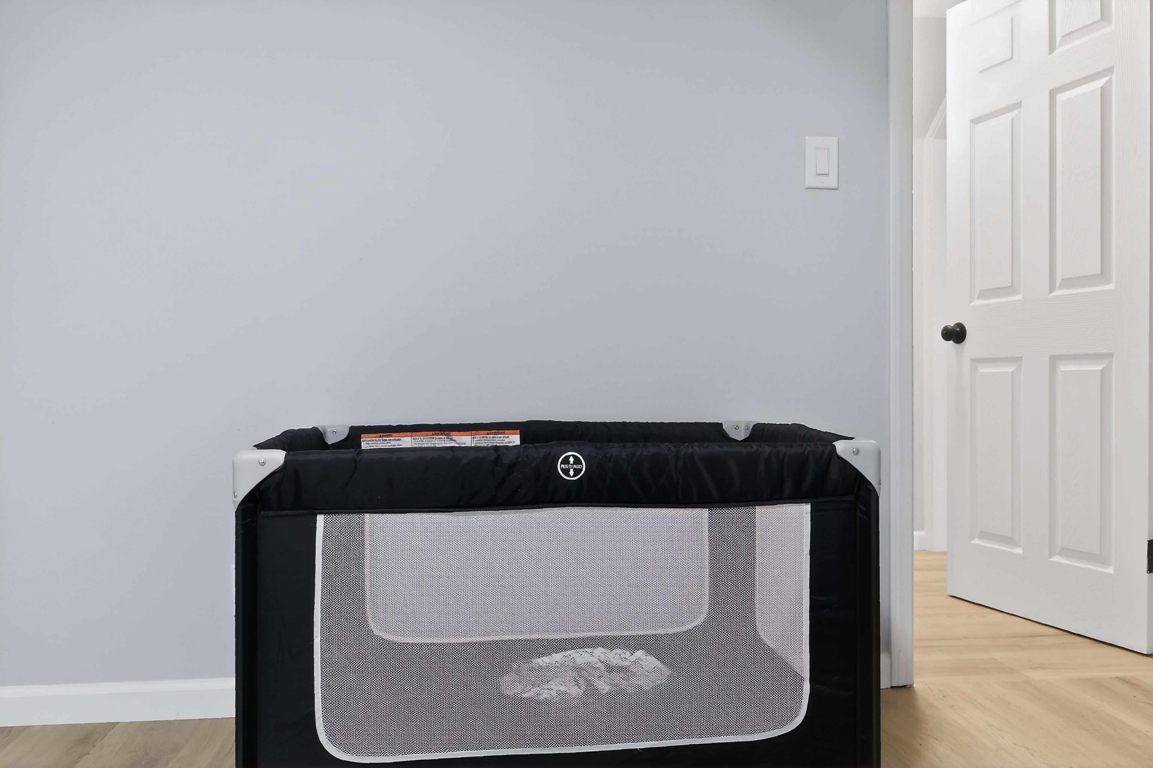 Une pièce avec une porte blanche, un mur gris et un enclos de jeu noir et gris pour animaux de compagnie.