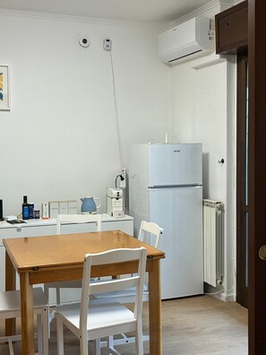 Una cocina con un refrigerador blanco, una cafetera y un hervidor sobre una encimera blanca.