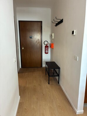 Un pasillo con puerta de madera, extintor, una mesita y teléfono en la pared.