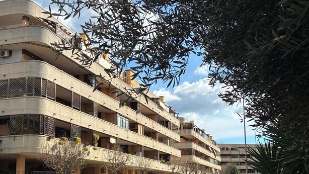 Um edifício residencial com vários andares, varandas, carros estacionados e áreas verdes.