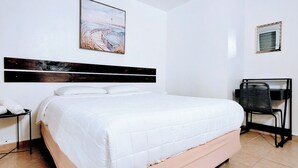 Ein Hotelzimmer mit Bett, Schreibtisch, Stuhl, kleinem Tisch mit Telefon und einem Bild an der Wand.