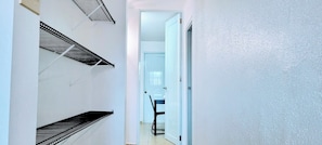 A hallway with black metal shelves, a white door, and a glimpse of a room with a chair and table. - Cofresi Inn - In the Heart of Cabo Rojo, PR (Cabo Rojo)