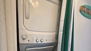 Eine kompakte Wasch- und Trockenereinheit mit Bedienfeld, einem kleinen Stauraum und einem grün gestreiften Vorhang.