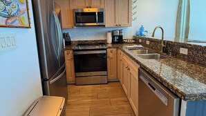 Eine kompakte Küche mit Holzschränken, einem Edelstahl-Kühlschrank, einer Mikrowelle, einem Backofen, einem Geschirrspüler und einer Arbeitsplatte aus Granit.