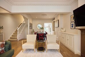 A spacious living room with a staircase, a dining area, and a fireplace. - Host My Nest: Spacious 4BR House with Garden (London)