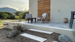 Um pátio com duas cadeiras, uma mesa e uma porta de madeira, com vista para a paisagem.