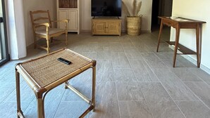 Uma sala de estar ampla com teto de madeira, uma televisão, uma mesa de vime e um armário.