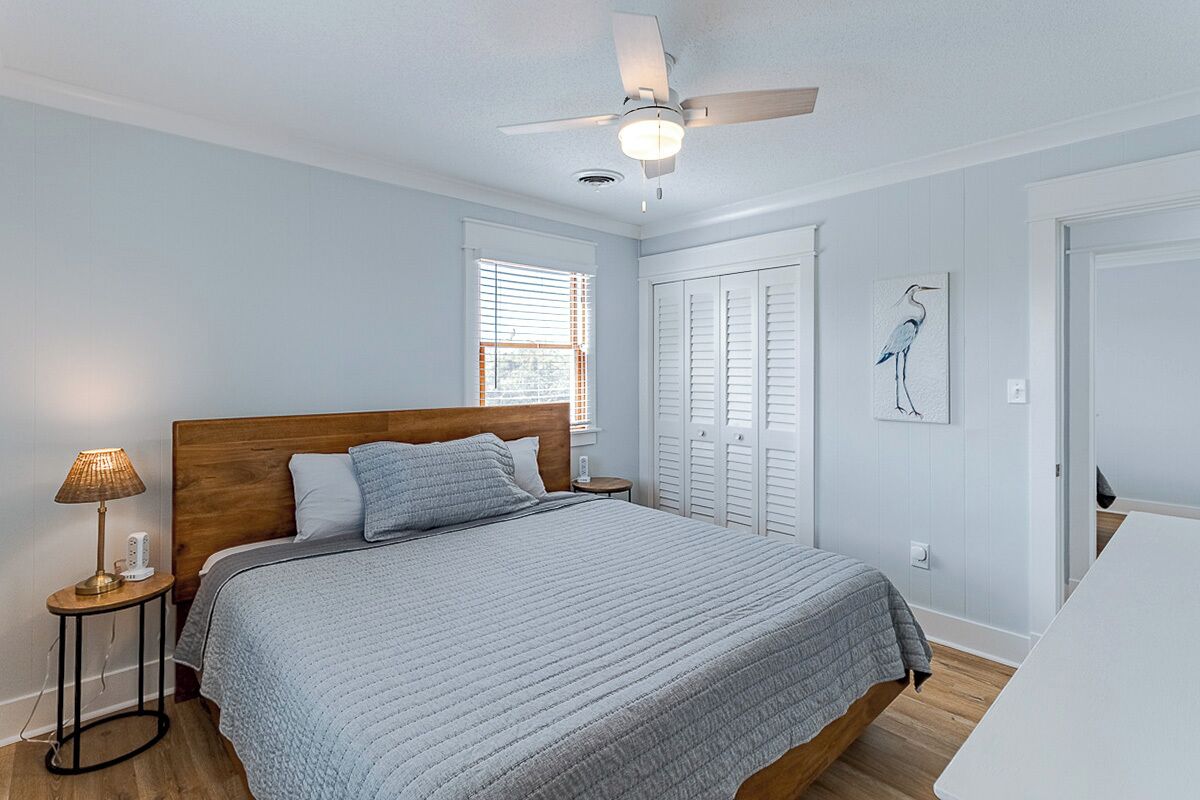 A bedroom with a bed, a ceiling fan, a nightstand, a lamp, and a window.