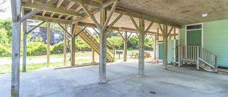 An open pavilion with a concrete floor and wooden beams, a green door, and a staircase leading to a covered area.