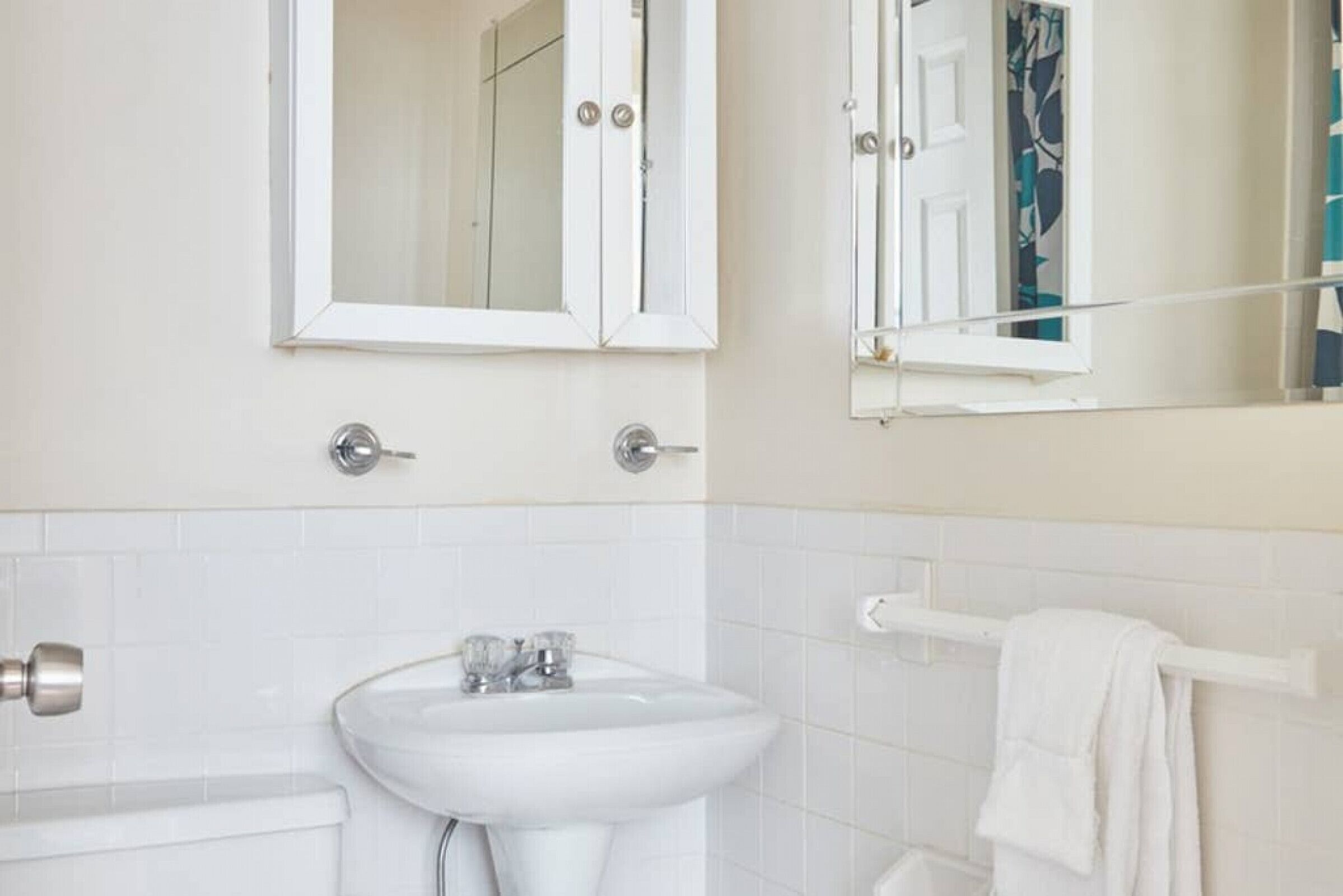 A bathroom with a white sink, two mirrors, and a towel rack.