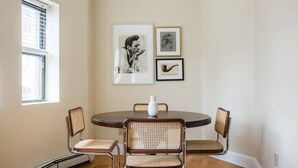 A dining area with a round table, four wicker chairs, and framed artwork on the wall. - Walk everywhere - Seaport, North End, Beacon Hill.  Steps from MBTA public transit.  Keyless Entry! (Boston)