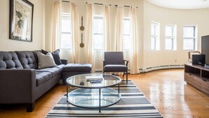 A living room with a sofa, armchair, and two round tables. - Walk everywhere - Seaport, North End, Beacon Hill.  Steps from MBTA public transit.  Keyless Entry! (Boston)