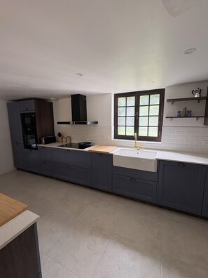 Een moderne keuken met een groot kookeiland, een inbouwoven en een raam dat voor natuurlijk licht zorgt.