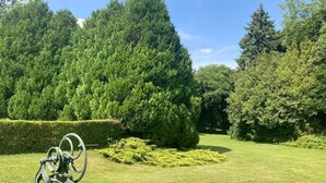 A well-maintained garden with a variety of trees and shrubs, a metal sculpture, and a neatly trimmed hedge. - Normandy country house (pool+tennis) 16 pers (Brionne)
