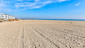 Een strand met een houten pier en een wit gebouw met balkons.